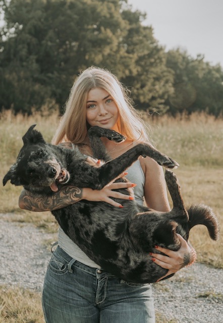 Alexa holding one of her dogs in a sunlit field